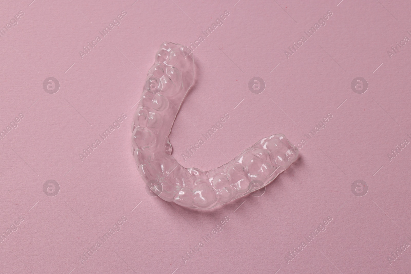 One clear aligner on pink background, top view Photo of One clear aligner on pink background, top view
