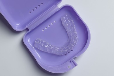 Photo of One clear aligner in retainer case on light grey background, top view
