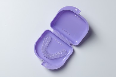 Photo of One clear aligner in retainer case on light grey background, top view