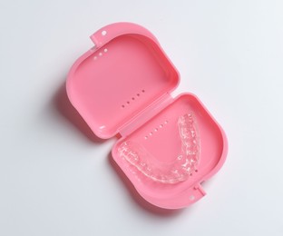 Photo of One clear aligner in retainer case on light grey background, top view