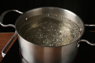 Photo of Metal pot with boiling water on stove in kitchen, closeup
