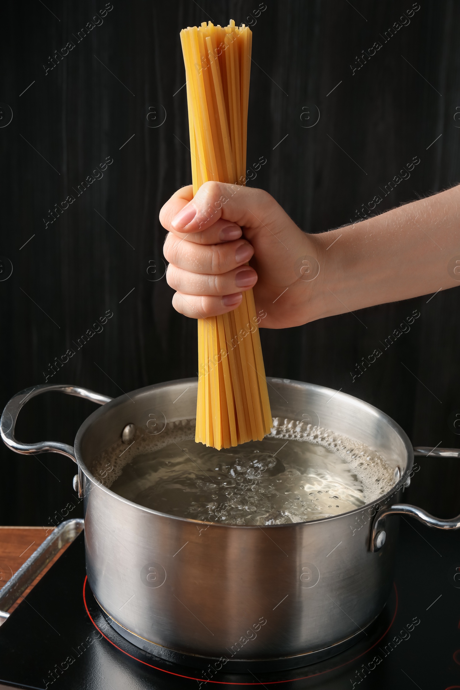 Woman putting tagliatelle pasta into pot on electric stove in kitchen, closeup Photo of Woman putting tagliatelle pasta into pot on electric stove in kitchen, closeup