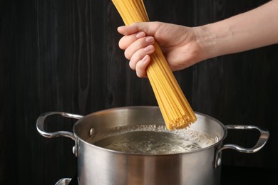 Photo of Woman putting tagliatelle pasta into pot on electric stove in kitchen, closeup