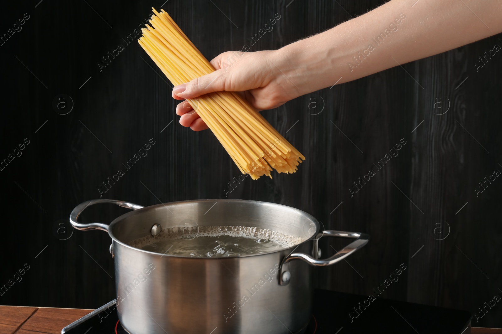 Woman putting tagliatelle pasta into pot on electric stove in kitchen, closeup Photo of Woman putting tagliatelle pasta into pot on electric stove in kitchen, closeup