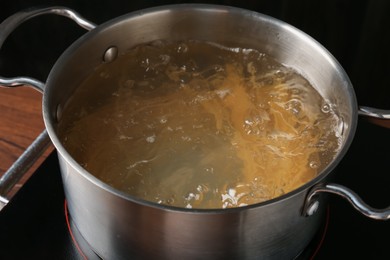 Photo of Fresh tagliatelle pasta boiling in pot with water on electric stove, closeup