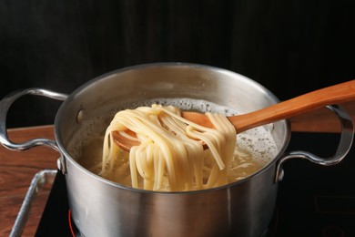 Photo of Taking boiled tagliatelle pasta with spoon from pot on electric stove, closeup