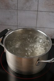 Photo of Metal pot with boiling water on stove in kitchen, closeup