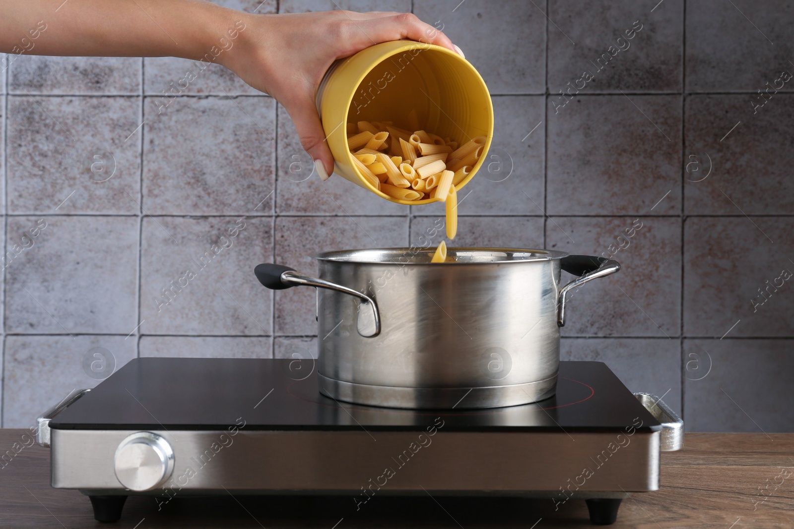 Woman putting penne pasta into pot with boiling water on electric stove, closeup Photo of Woman putting penne pasta into pot with boiling water on electric stove, closeup