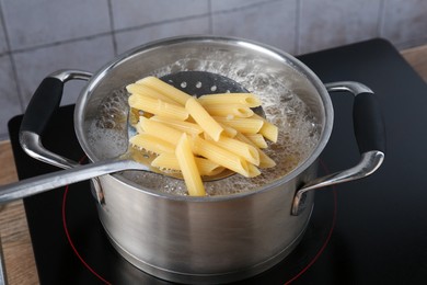 Photo of Taking cooked penne pasta from pot with boiling water on electric stove, closeup