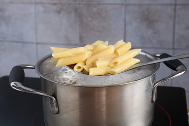 Photo of Taking cooked penne pasta from pot with boiling water on electric stove, closeup
