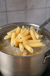 Photo of Taking cooked penne pasta from pot with boiling water on electric stove, closeup