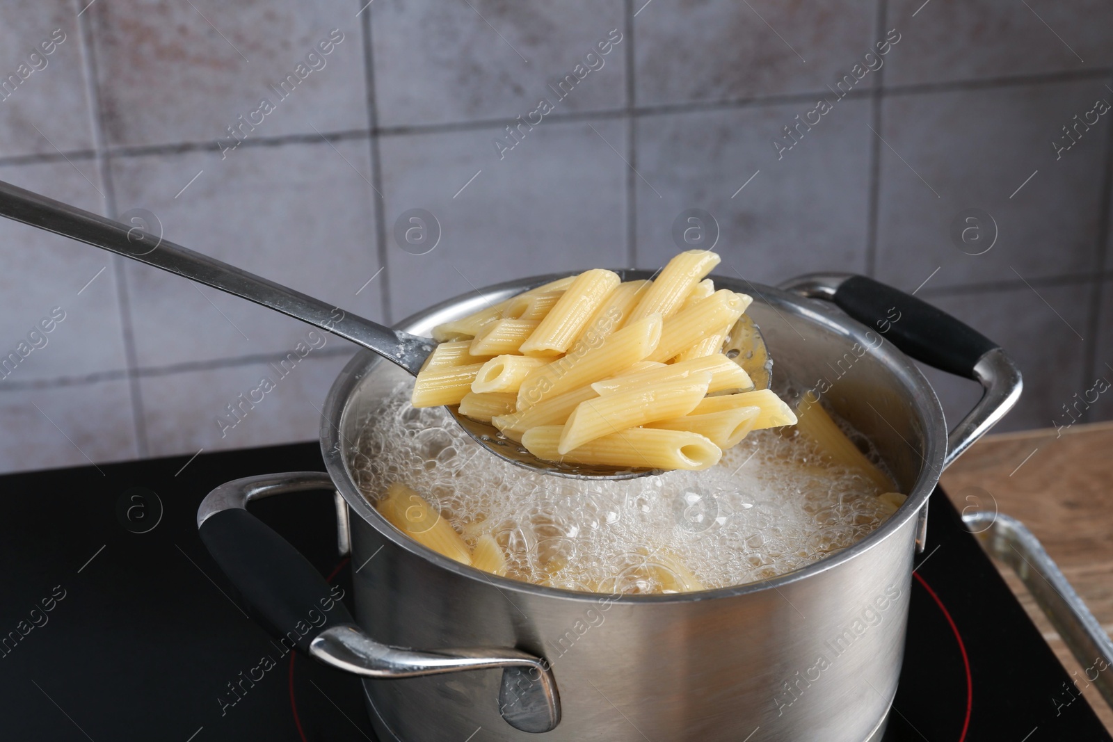 Taking cooked penne pasta from pot with boiling water on electric stove, closeup Photo of Taking cooked penne pasta from pot with boiling water on electric stove, closeup