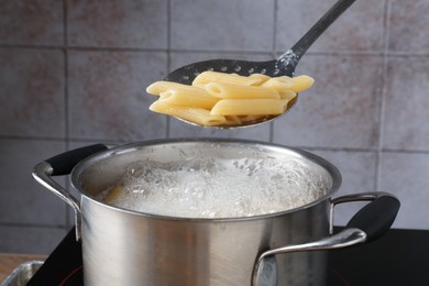 Photo of Taking cooked penne pasta from pot with boiling water on electric stove, closeup