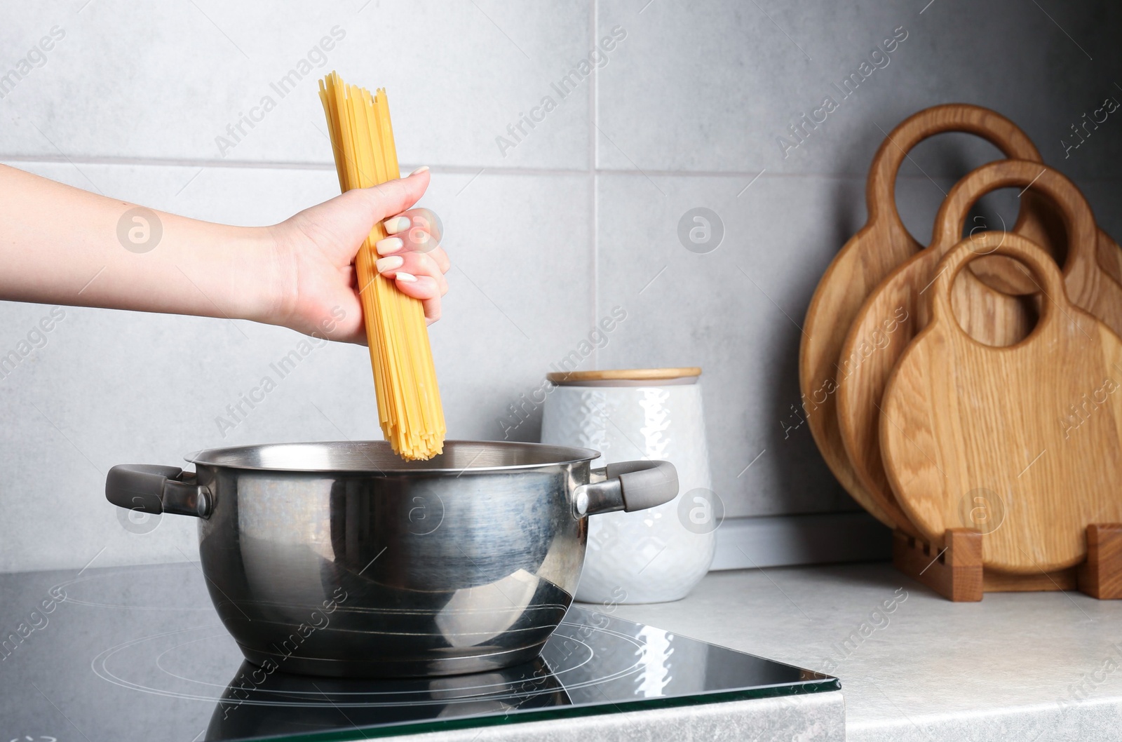Photo of Woman putting tagliatelle pasta into pot on electric stove in kitchen, closeup