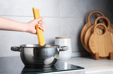 Photo of Woman putting tagliatelle pasta into pot on electric stove in kitchen, closeup