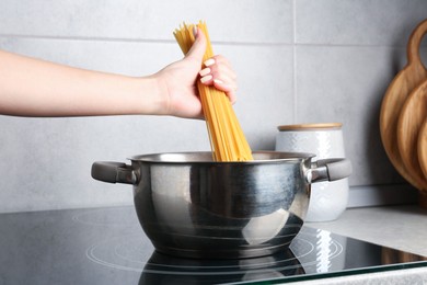 Photo of Woman putting tagliatelle pasta into pot on electric stove in kitchen, closeup