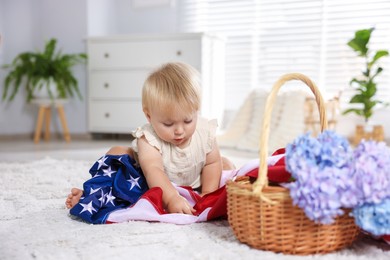 Photo of Cute little child with flag of USA and wicker basket of hydrangea flowers on floor at home