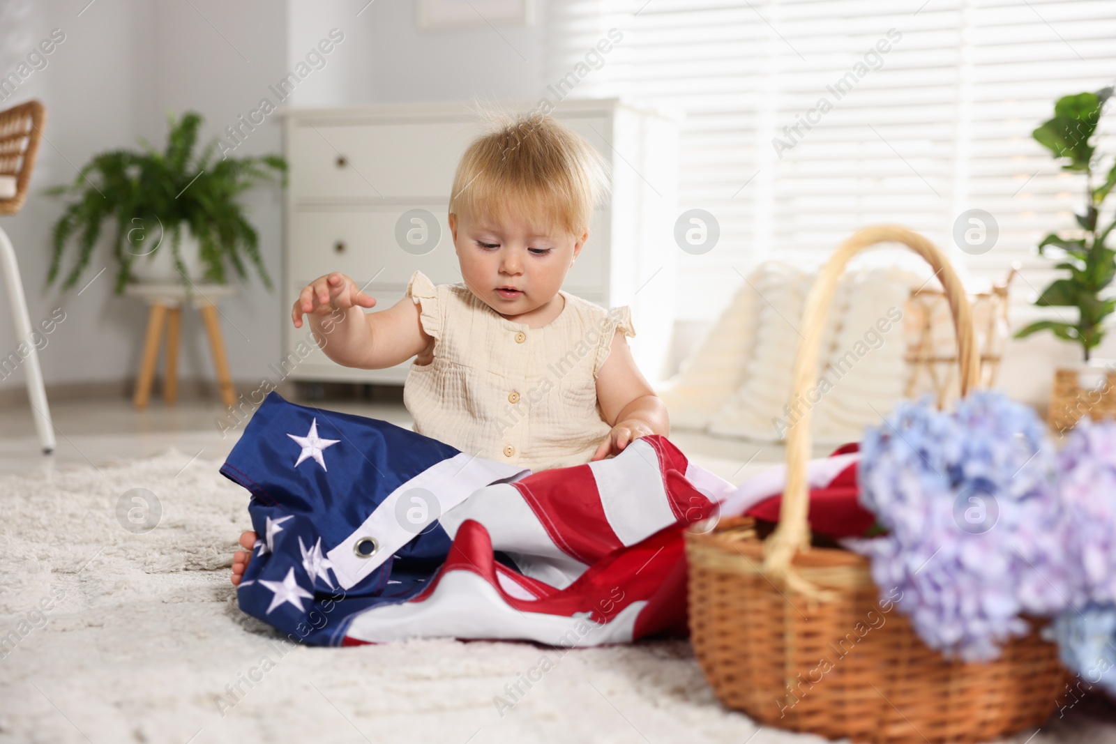 Photo of Cute little child with flag of USA and wicker basket of hydrangea flowers on floor at home