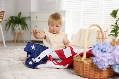 Photo of Cute little child with flag of USA and wicker basket of hydrangea flowers on floor at home