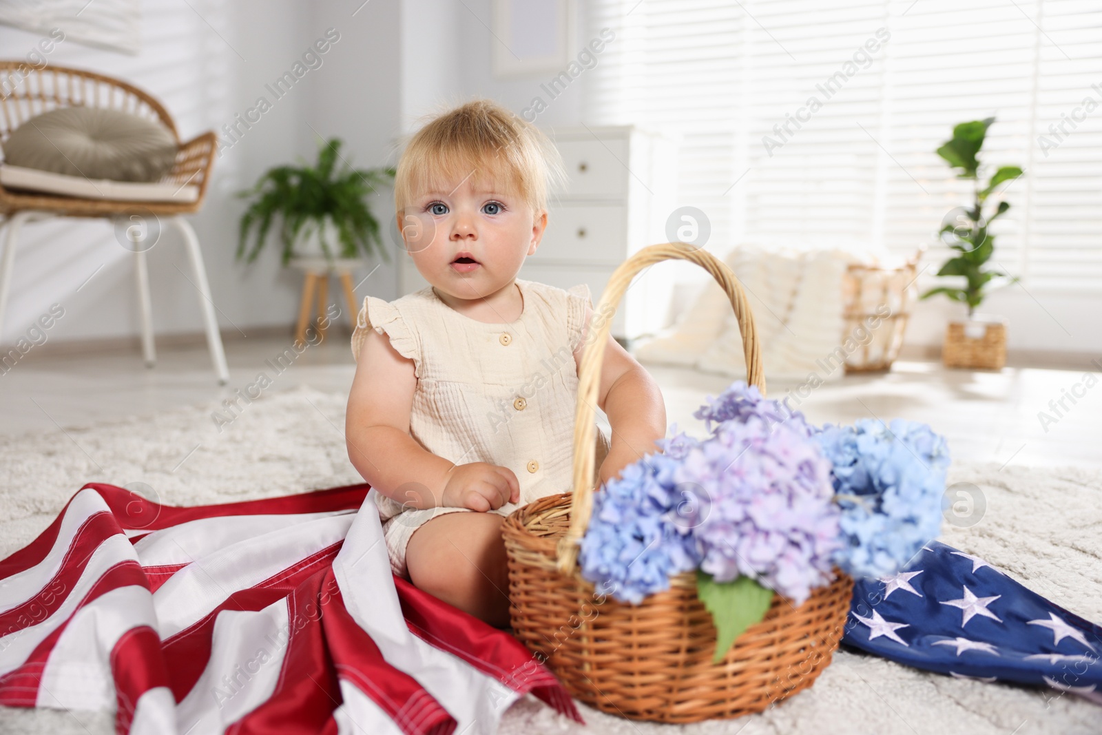 Photo of Cute little child with flag of USA and wicker basket of hydrangea flowers on floor at home