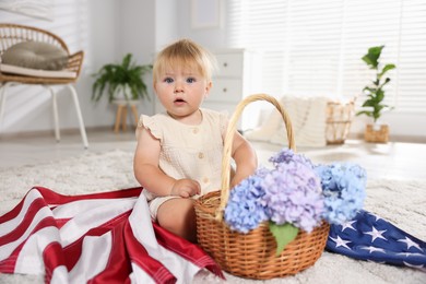 Photo of Cute little child with flag of USA and wicker basket of hydrangea flowers on floor at home