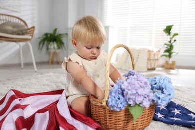 Photo of Cute little child with flag of USA and wicker basket of hydrangea flowers on floor at home