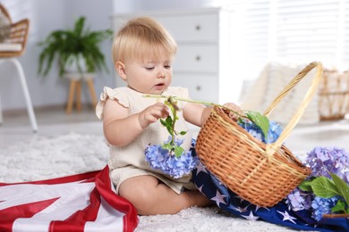 Photo of Cute little child with flag of USA and wicker basket of hydrangea flowers on floor at home