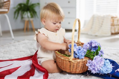 Photo of Cute little child with flag of USA and wicker basket of hydrangea flowers on floor at home