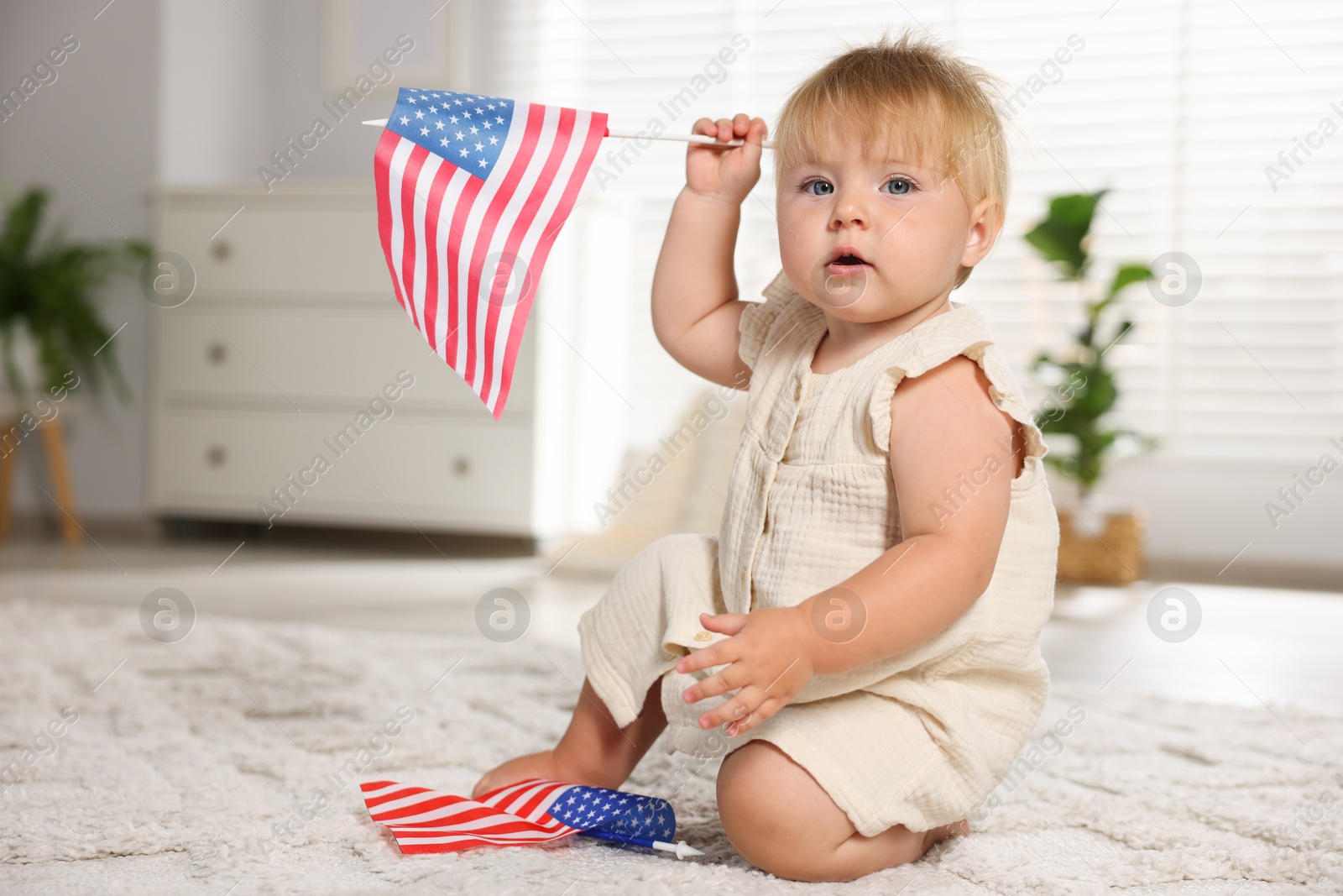 Photo of Cute little child with flags of USA on floor at home, space for text
