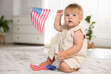 Photo of Cute little child with flags of USA on floor at home, space for text