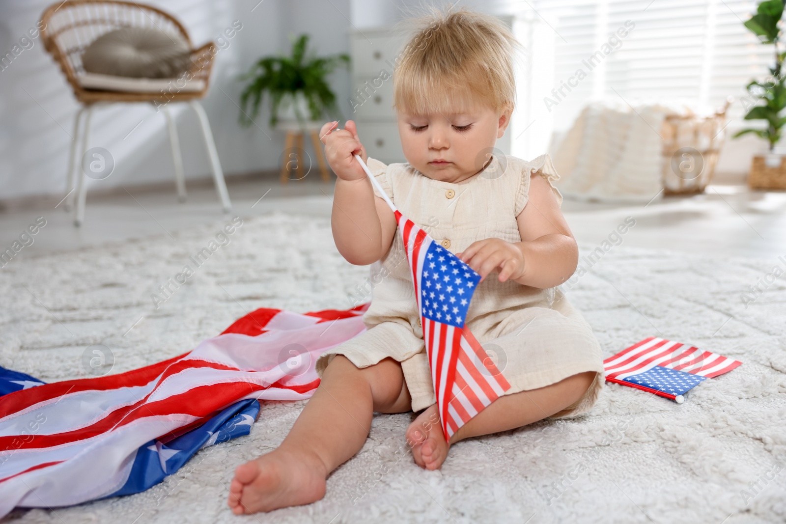 Photo of Cute little child with flags of USA on floor at home