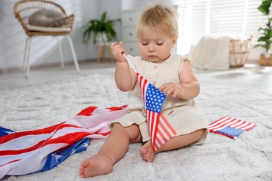 Photo of Cute little child with flags of USA on floor at home