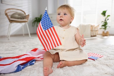 Photo of Cute little child with flags of USA on floor at home