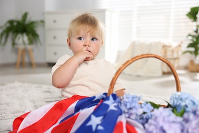 Photo of Cute little child with flag of USA and wicker basket of hydrangea flowers on floor at home