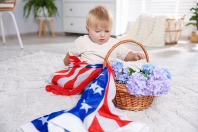 Photo of Cute little child with flag of USA and wicker basket of hydrangea flowers on floor at home