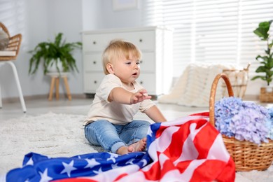 Photo of Cute little child with flag of USA and wicker basket of hydrangea flowers on floor at home