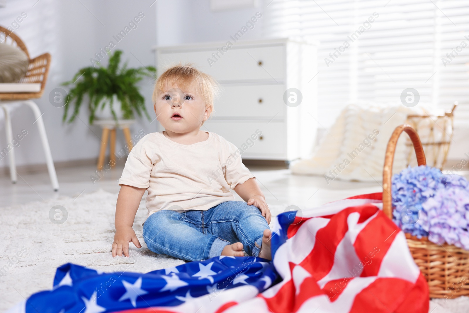 Photo of Cute little child with flag of USA and wicker basket of hydrangea flowers on floor at home