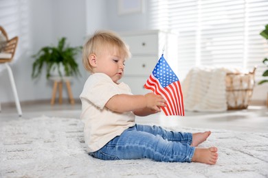 Photo of Cute little child with flag of USA on floor at home