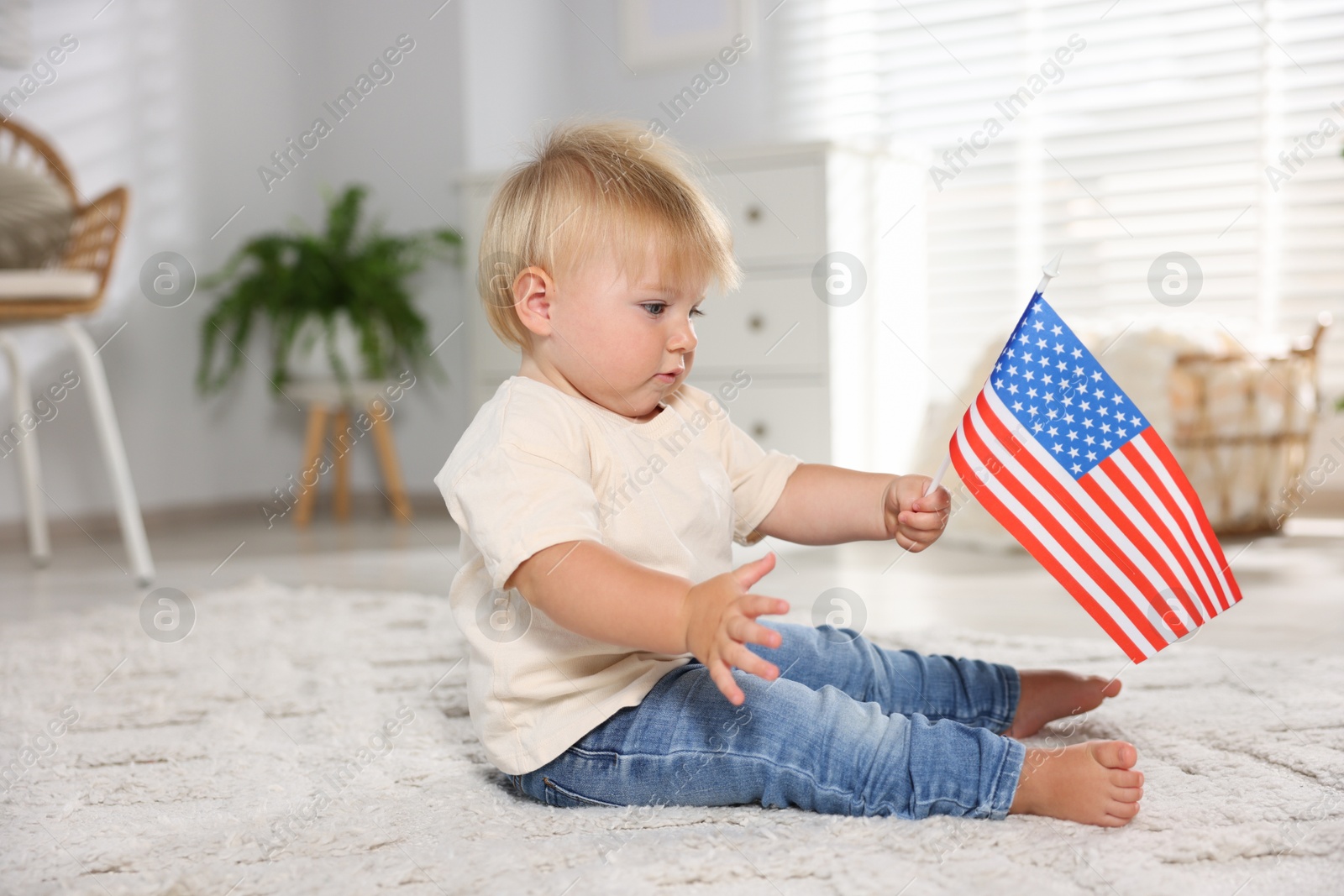 Photo of Cute little child with flag of USA on floor at home