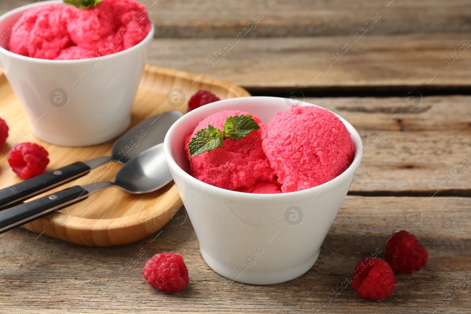 Photo of Delicious raspberry sorbet with mint in bowl and fresh berries on wooden table, closeup