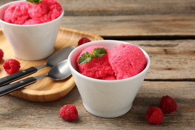 Photo of Delicious raspberry sorbet with mint in bowl and fresh berries on wooden table, closeup