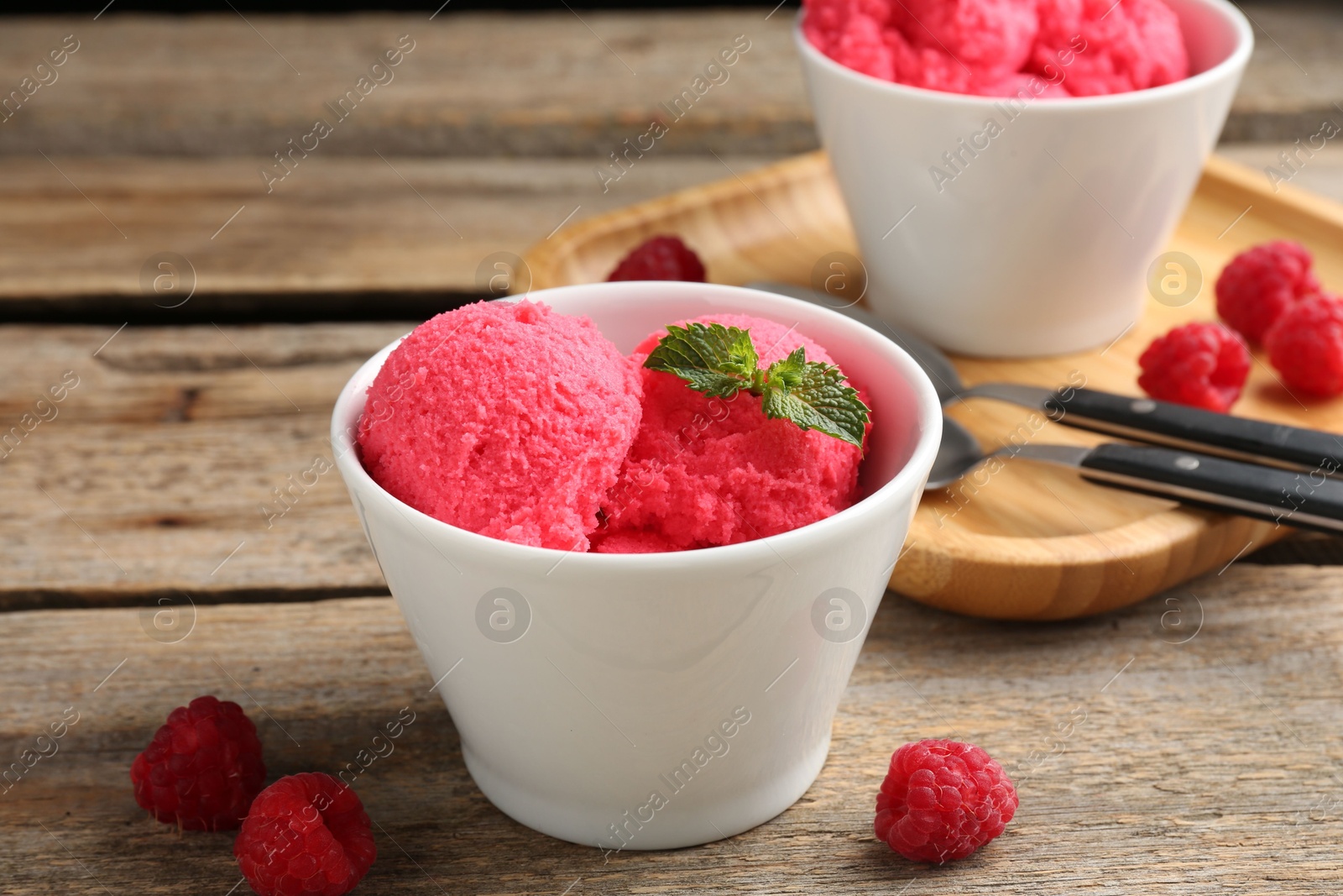 Photo of Delicious raspberry sorbet with mint in bowl and fresh berries on wooden table, closeup