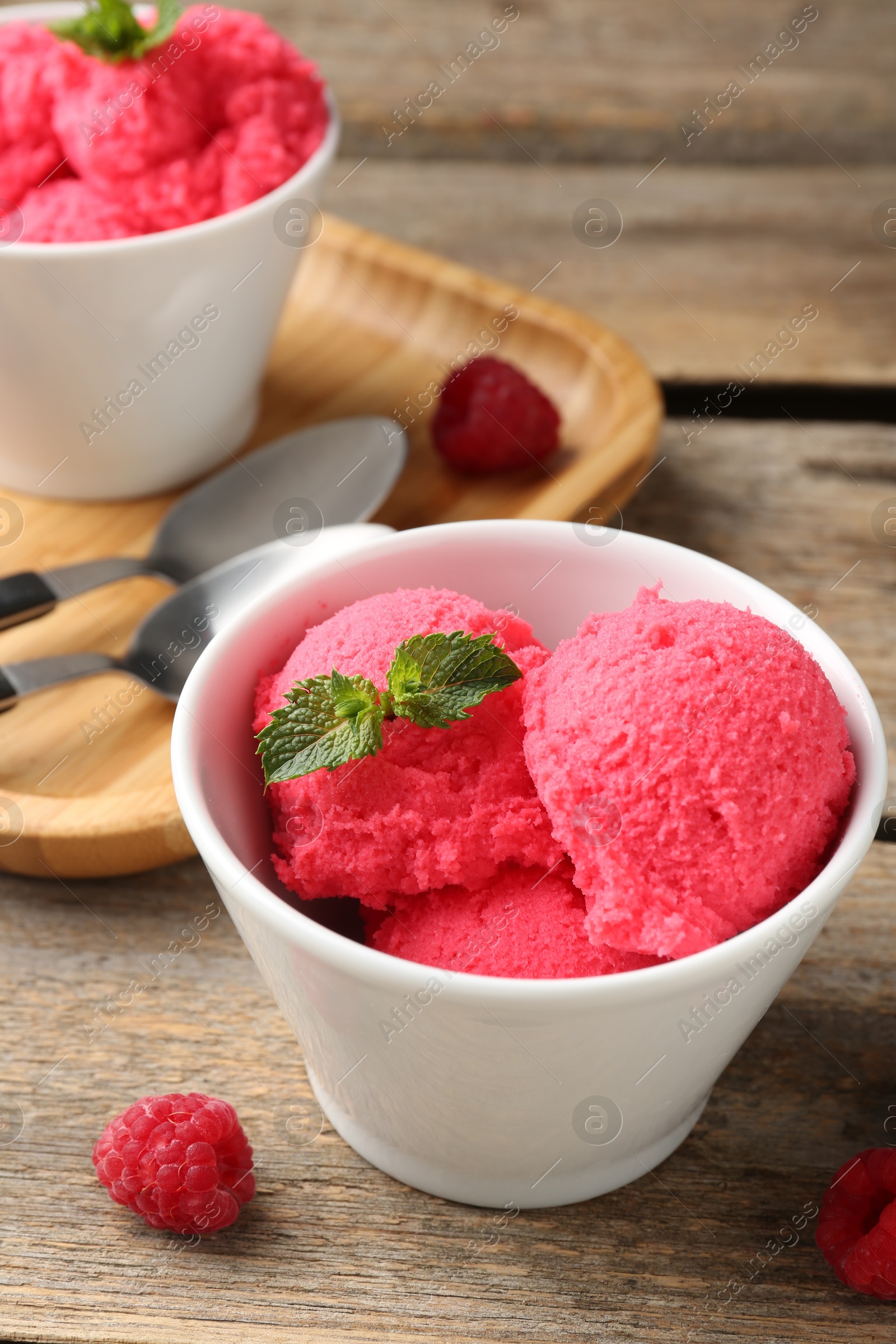 Photo of Delicious raspberry sorbet with mint in bowl and fresh berries on wooden table, closeup