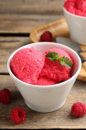 Photo of Delicious raspberry sorbet with mint in bowl and fresh berries on wooden table, closeup