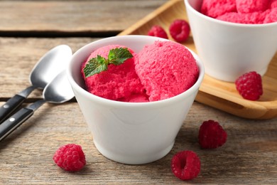 Photo of Delicious raspberry sorbet with mint in bowl and fresh berries on wooden table, closeup