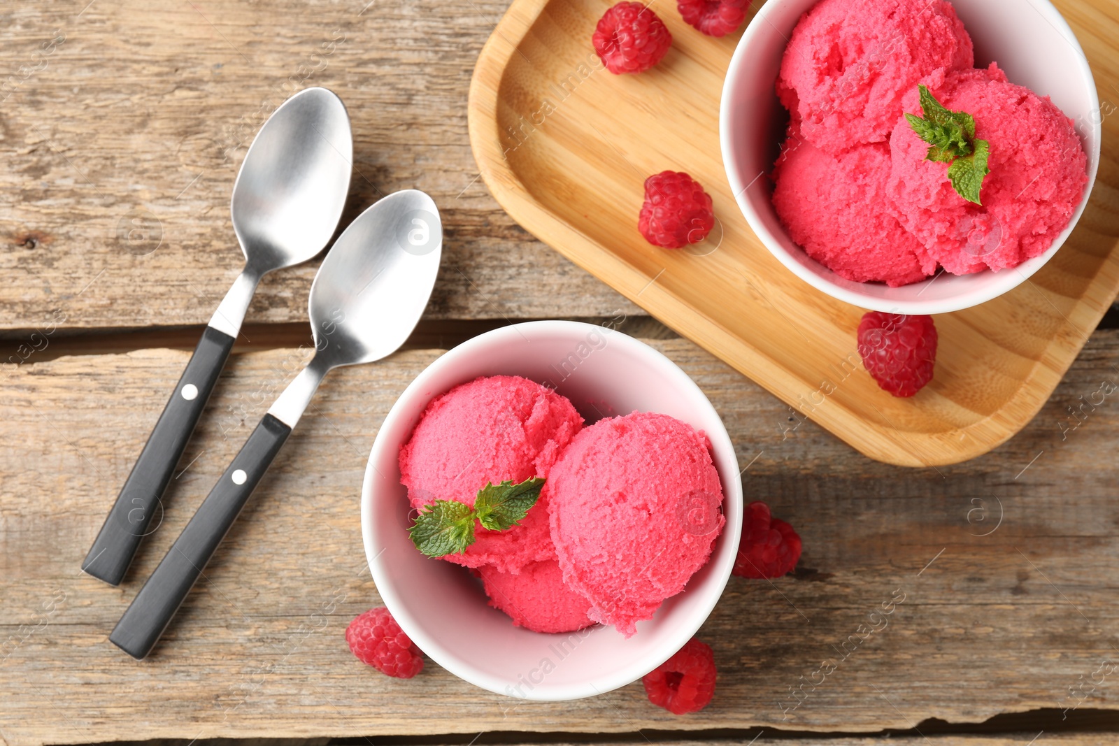 Photo of Delicious raspberry sorbet with mint in bowls, spoons and fresh berries on wooden table, flat lay