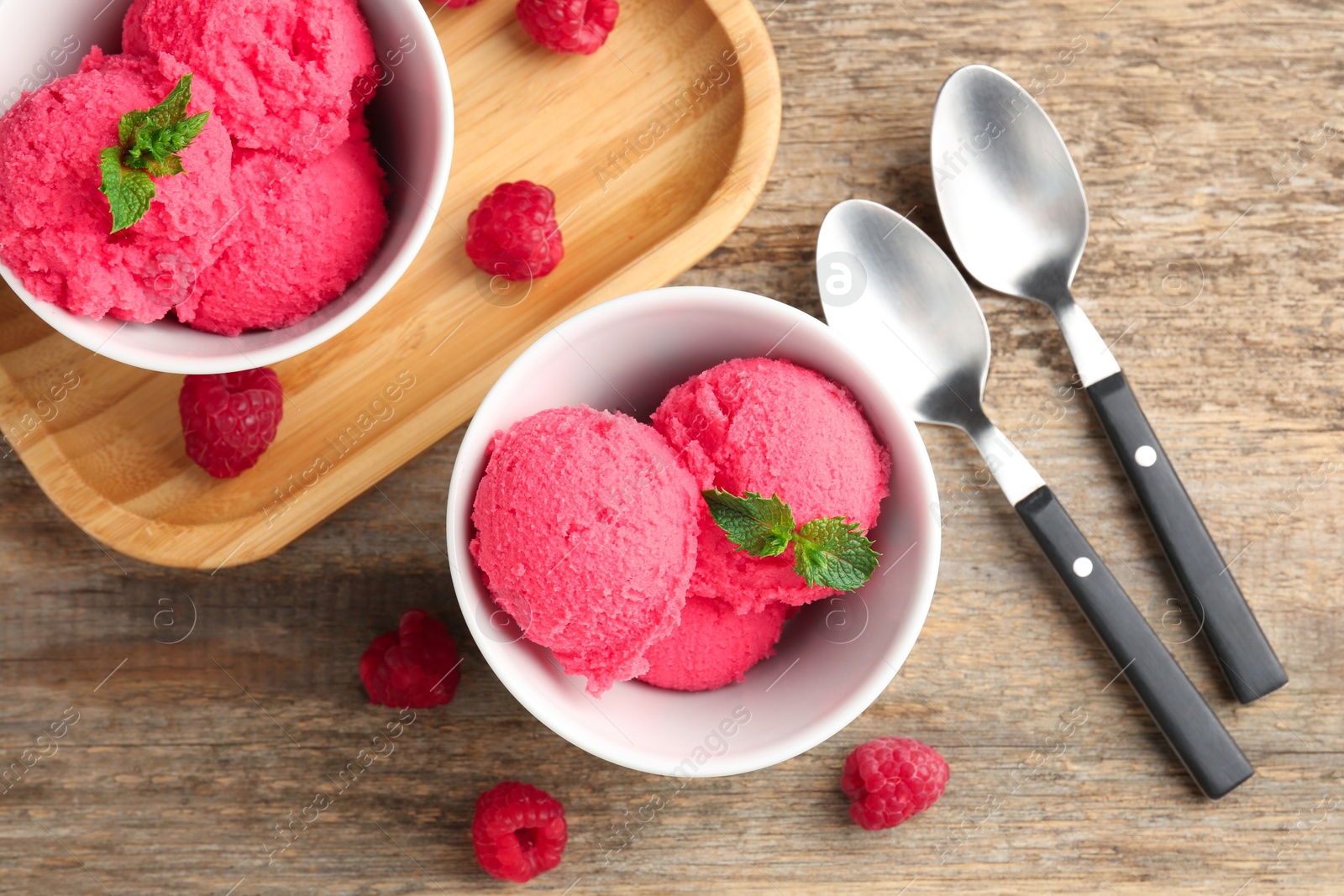 Photo of Delicious raspberry sorbet with mint in bowls, spoons and fresh berries on wooden table, flat lay