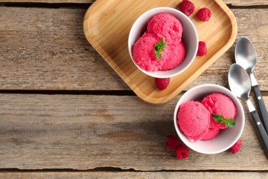 Photo of Delicious raspberry sorbet with mint in bowls, spoons and fresh berries on wooden table, flat lay. Space for text