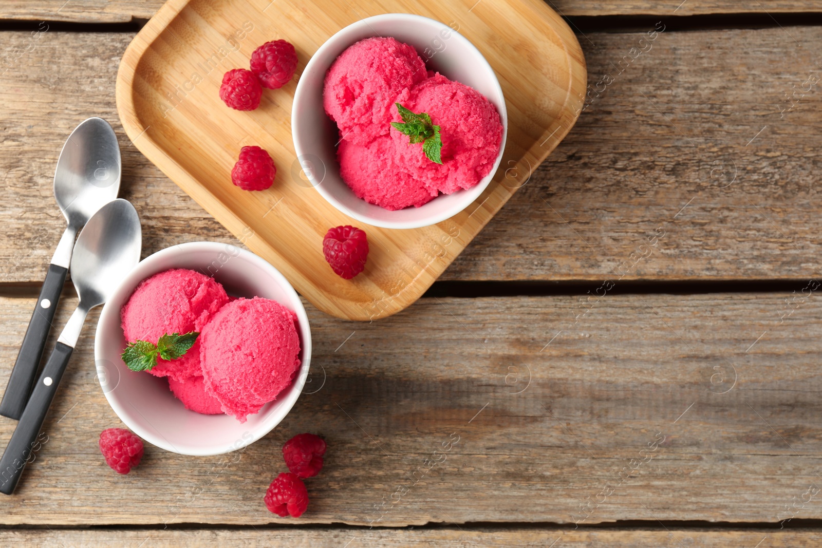 Photo of Delicious raspberry sorbet with mint in bowls, spoons and fresh berries on wooden table, flat lay. Space for text