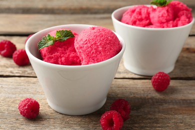 Photo of Delicious raspberry sorbet with mint in bowls and fresh berries on wooden table, closeup